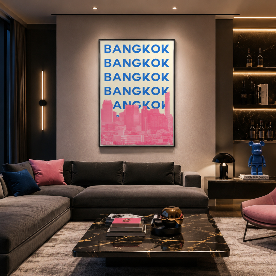 A framed wall art print featuring the word 'BANGKOK' repeated in blue text over a pink city skyline, displayed above a dark sectional sofa in a modern living room with city views at dusk.
