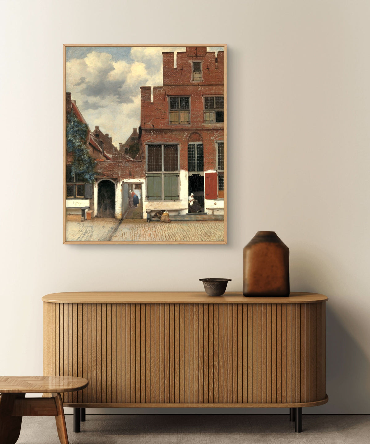 Framed painting of a street scene above a wooden sideboard with decorative items.