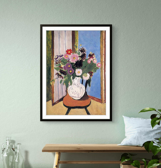 Framed artwork of a vase with flowers on a table against a window, hanging on a light green wall.