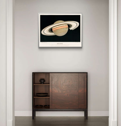 Framed artwork of Saturn on a wall above a wooden cabinet.