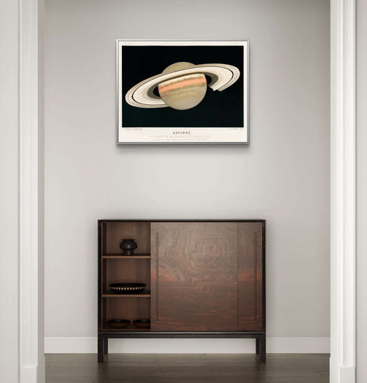 Framed artwork of Saturn on a wall above a wooden cabinet.