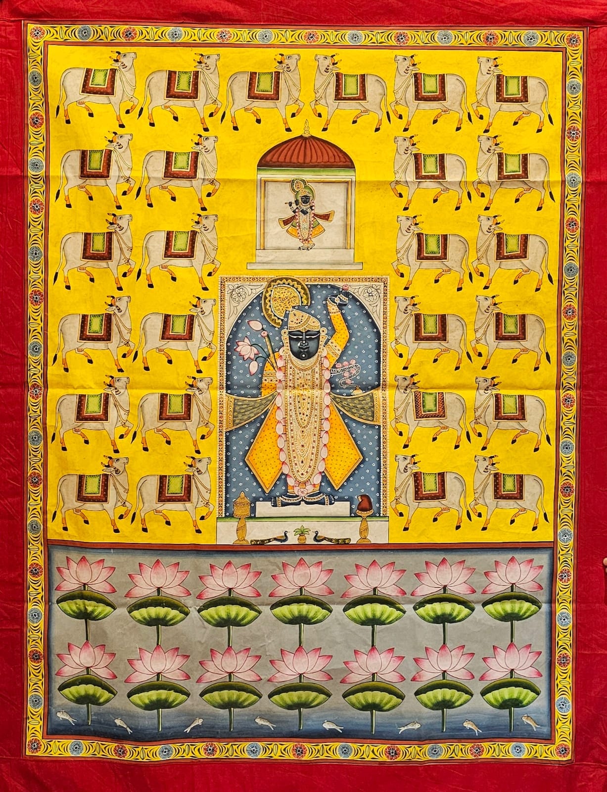 A hand-painted Pichwai Shrinathji fabric featuring a colorful depiction of cows, flowers, and a figure, set against a vibrant yellow background.