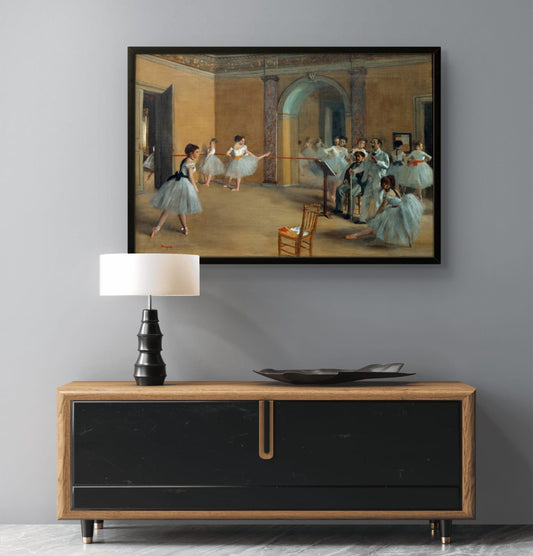 Framed painting of dancers in a studio above a wooden console table with a lamp and decorative items.