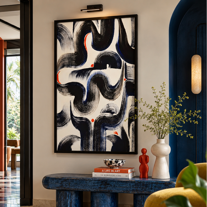 A large framed abstract wall art print with sweeping black, navy, and white brushstrokes and small orange-red accents, displayed in a styled interior hallway above a blue bench.
